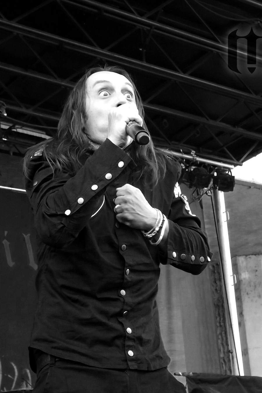 A singer in a dark shirt mid-song on an outdoor festival stage